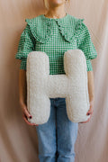 Boucle letter cushion H teddy letter pillow by bettys home held by young woman in green shirt on cream background 