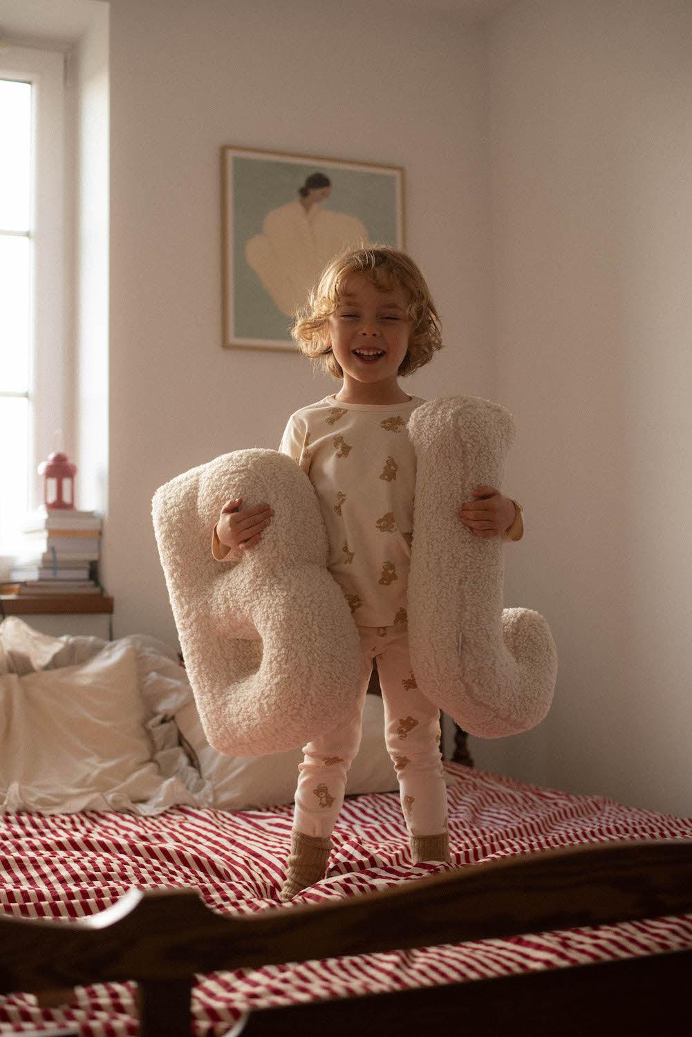 Boucle letter cushion B and J teddy pillow by bettys home held by little boy standing on bed 