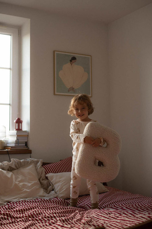 little boy standing on bed and holding boucle letter cushion B by bettys home 