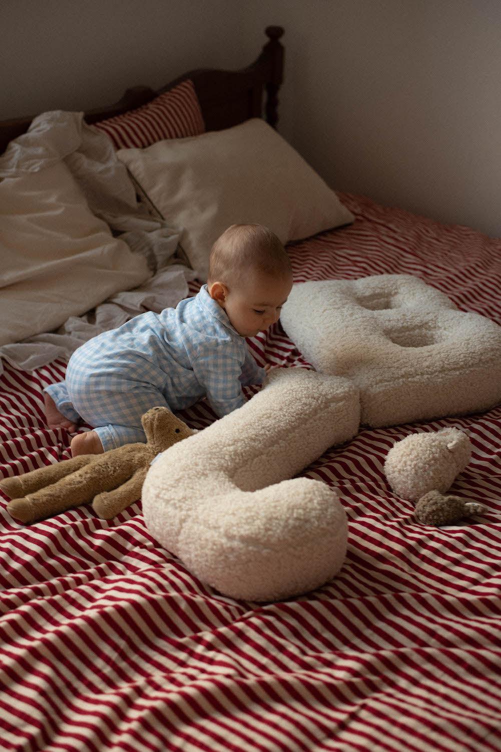 little baby boy in bed next to boucle letter cushion B and J teddy pillow by bettys home
