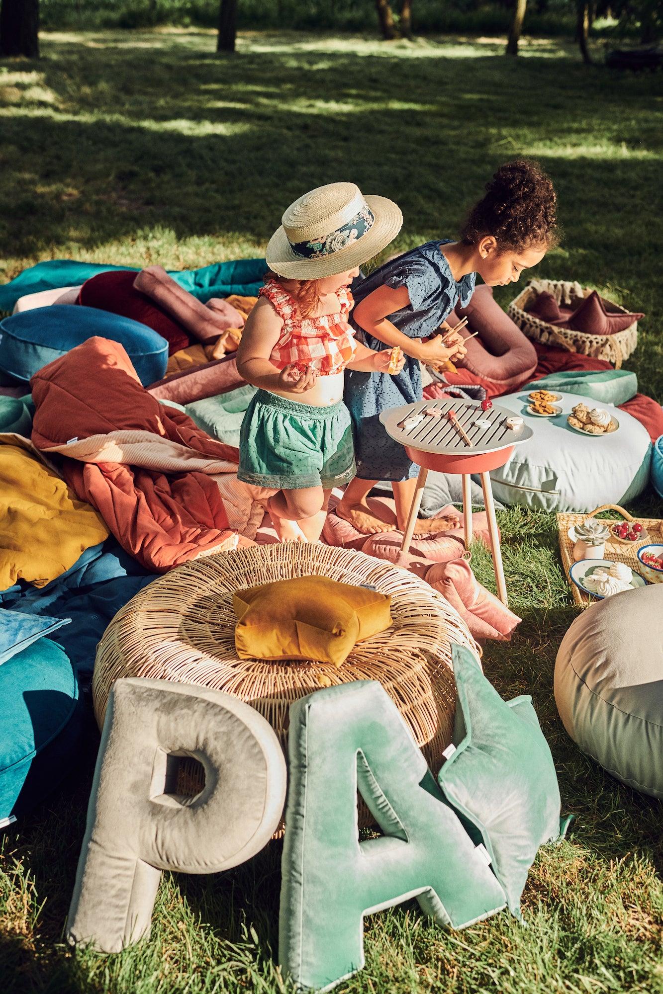 charming girl in garden during picnic with velvet letter cushion by bettys home